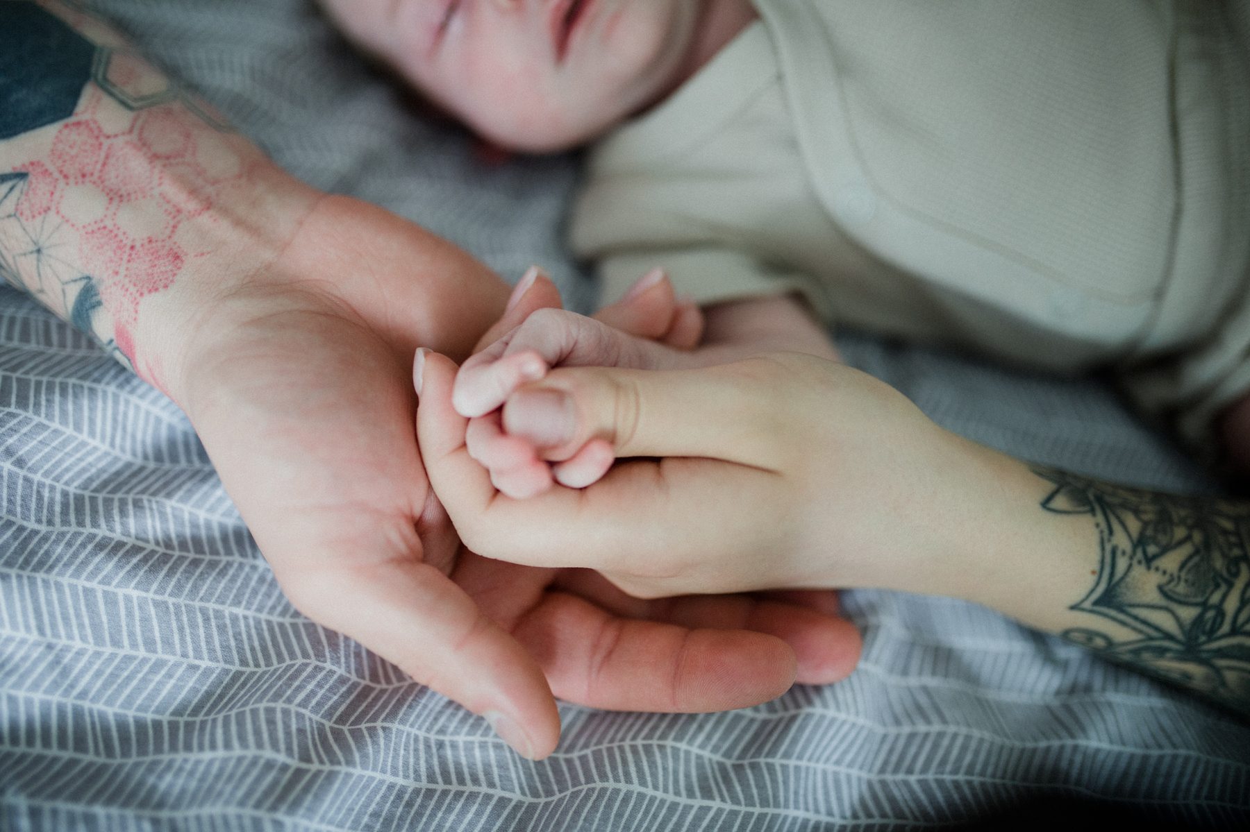 Baby hält Finger, Detail mit Tattoo